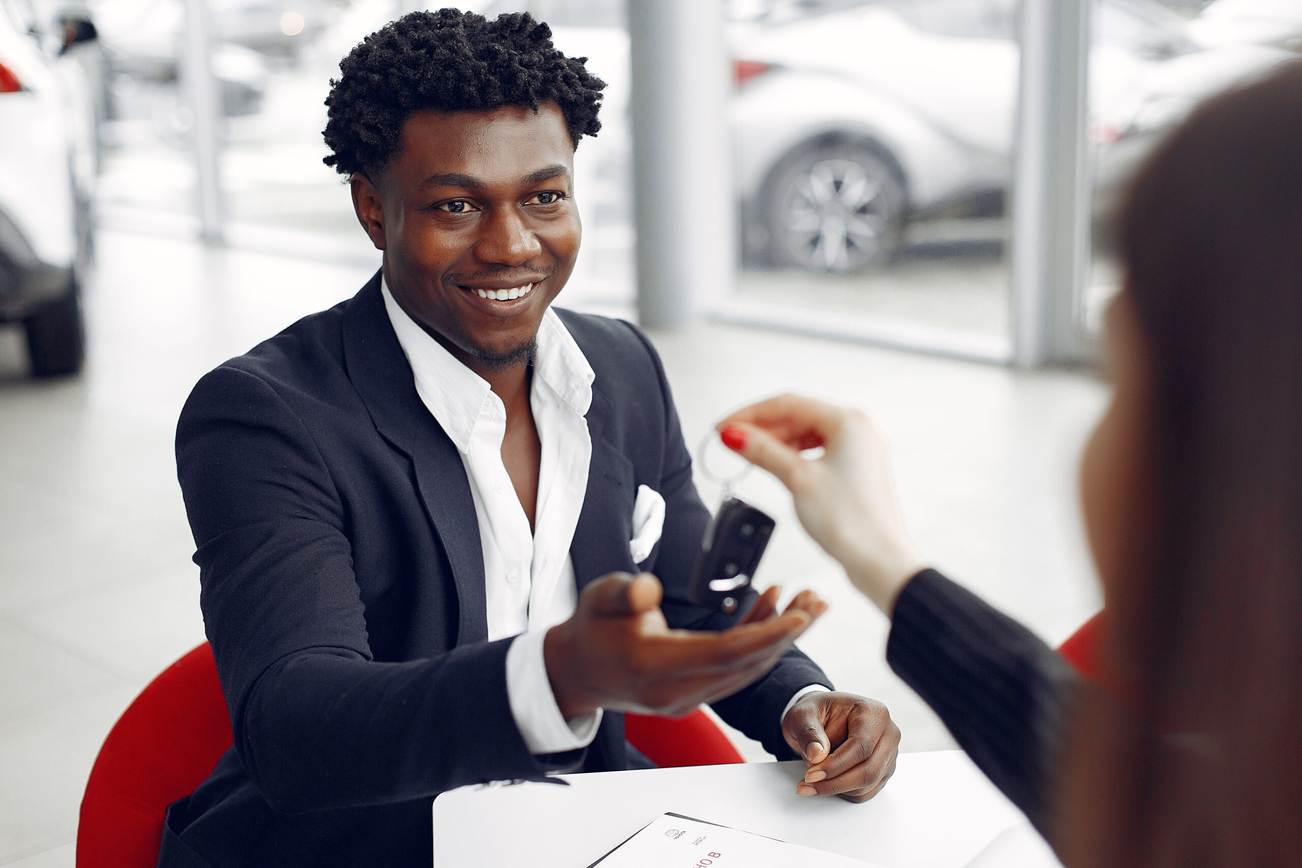 Man buying the car. Assistant helps to contract. Businessman in a car salon. Black male in a suit.